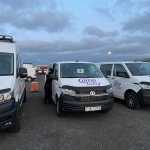 CampEasy Volkswagen campervans parked in a row at a rental facility during dusk, with a person loading equipment into one of the vans, preparing for a journey.