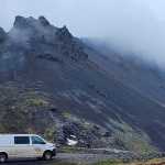 White CampEasy campervan parked on a gravel road in front of a dramatic, fog-covered mountain peak in Iceland, showcasing the van’s capability for highland adventures.