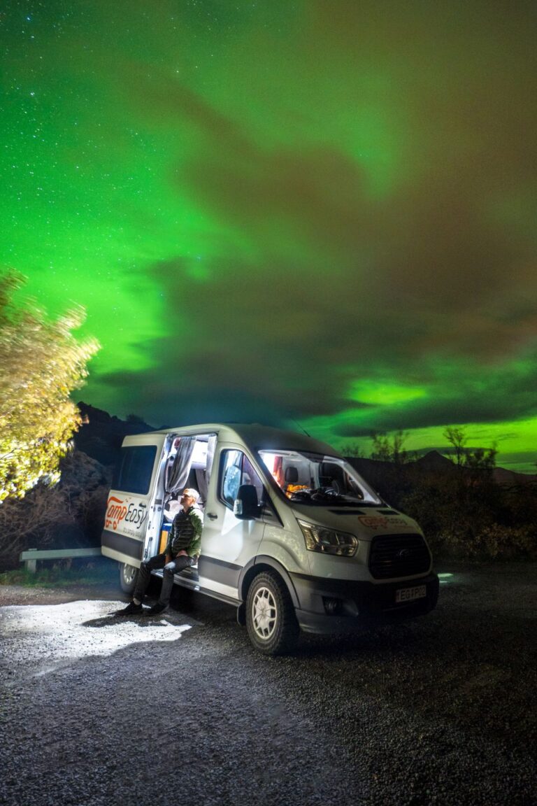 A campervan parked beneath vibrant Northern Lights in Iceland