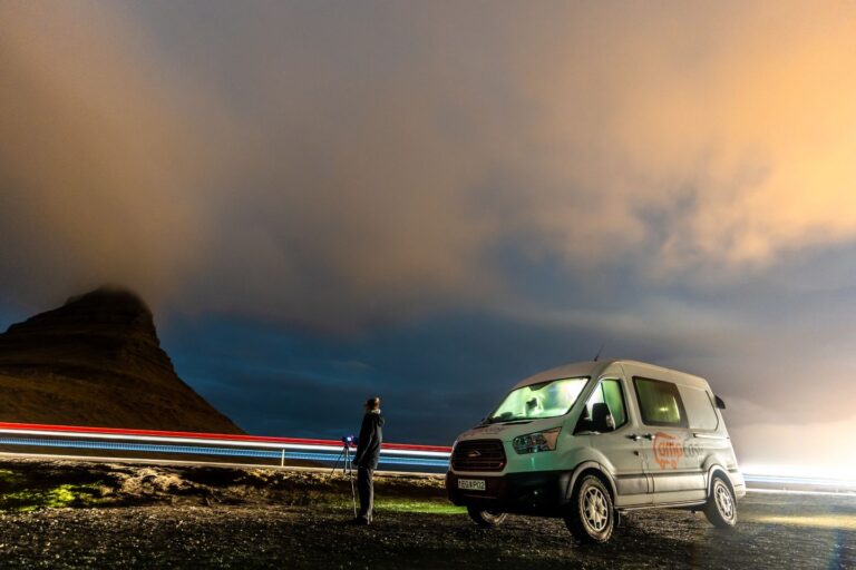 A campervan parked on a roadside at night, next to the famous Kirkjufell mountain in Iceland.