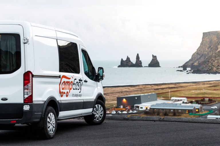 A white camping van parked on a parking with a view of city of Vik and famous Icelandic black beach.