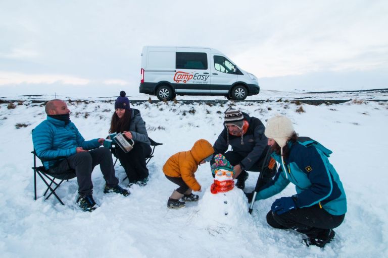 A family of five are spending their time on a snow next to the camper van.