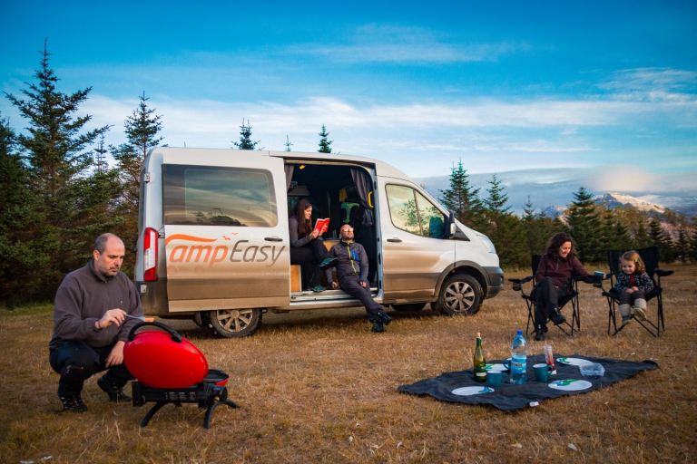 A family of five is resting between their journey through Iceland, resting and preparing a meal in the camping field surrounded by trees.