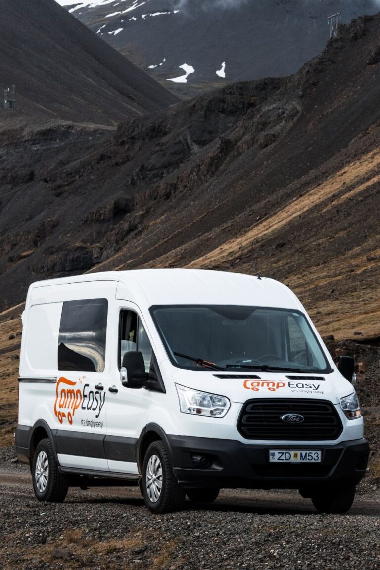 A white camping van parked on a dirt road surrounded by Icelandic landscape.