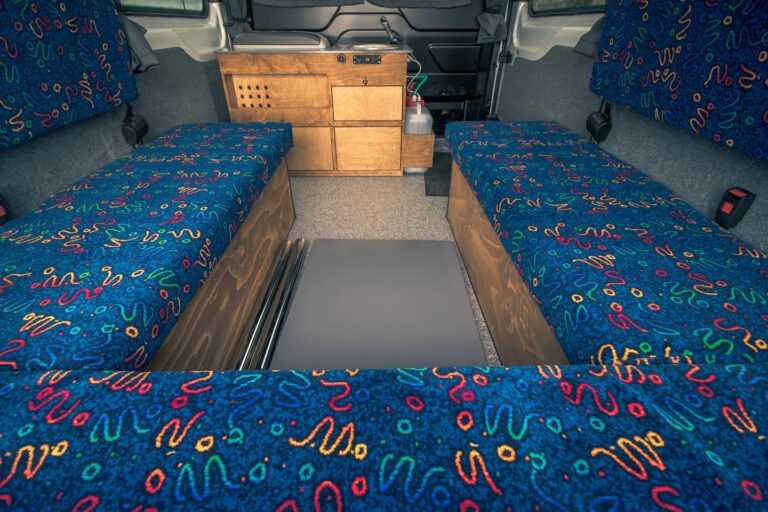 Interior view of a campervan with an unassembled table, sitting area and kitchen corner in the background.