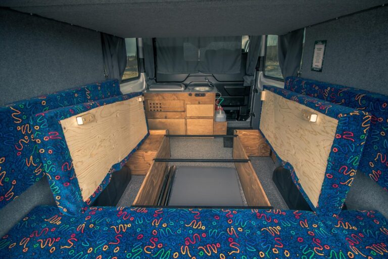 Interior view of a campervan with an unassembled bed and kitchen corner in the background.