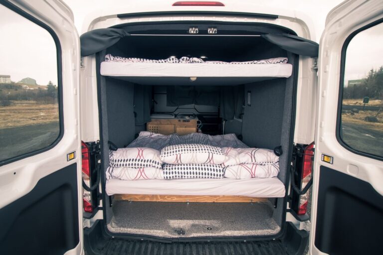A campervan with an open back door and set up the bedding inside.