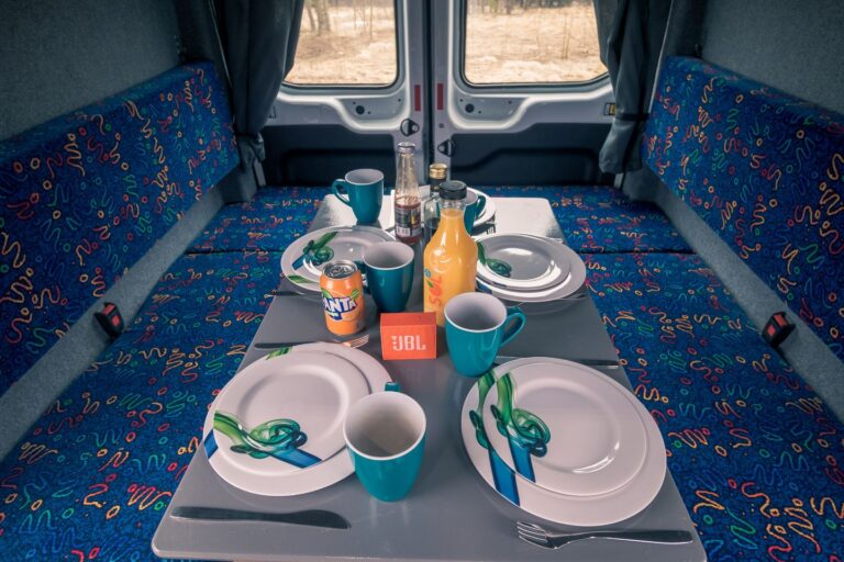 A table set inside a campervan, featuring plates, cups, and cutlery.