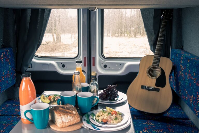 A guitar and a plate of food sit on a table inside a campervan, showcasing a cozy travel setting.