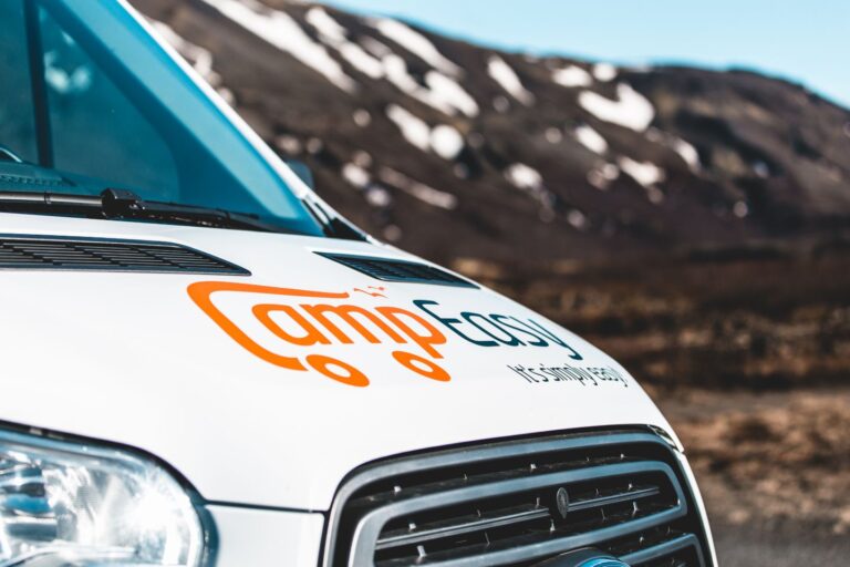 A white van with "Camp Easy" written on the front mask, parked in a scenic Icelandic landscape.