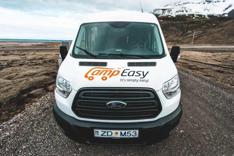 A front of white campervan parked on the gravel road near the mountains in Iceland.