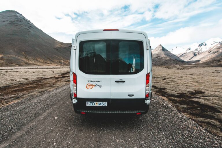A back of white campervan parked on the gravel road near the mountains in Iceland.