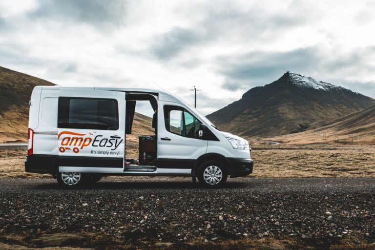 Parked campervan in Iceland on its side, parked against a scenic backdrop of mountains and fields.