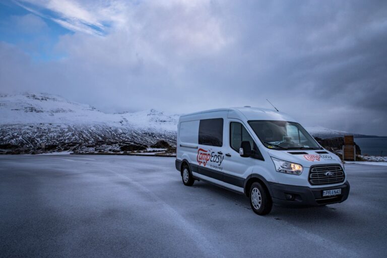 A camping van parked on a snowy road with mountains in the background