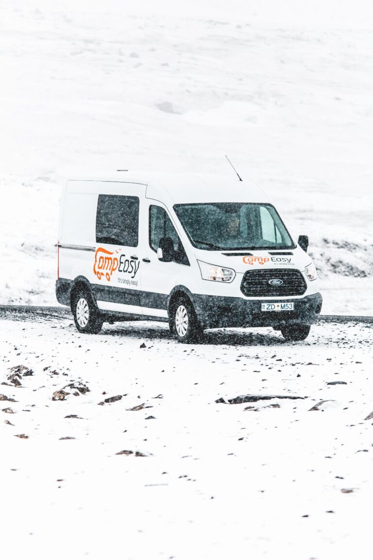A white campervan parked on a snow-covered road, with snowflakes falling around in Iceland.