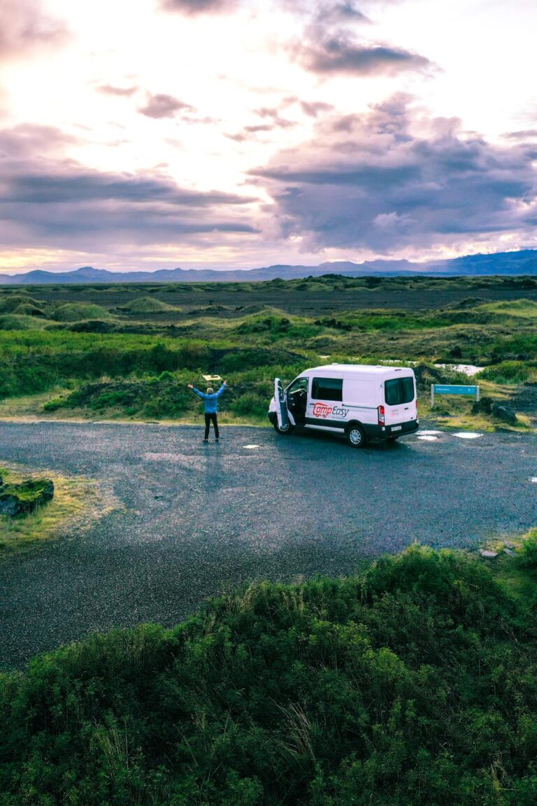 A campervan parked on a dirt road surrounded by lush green landscape in Iceland and mountains in the background.