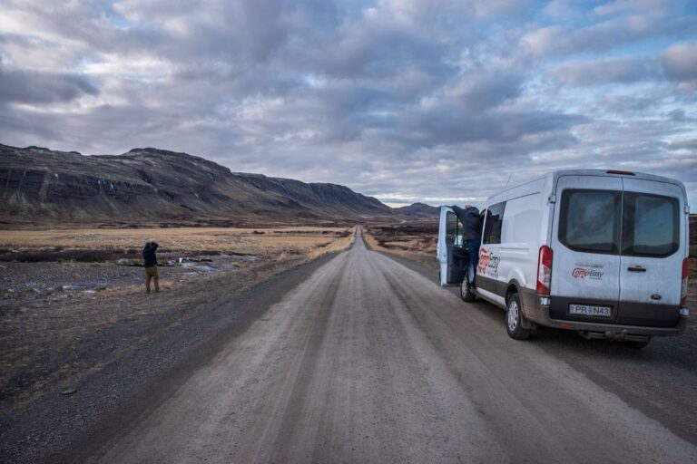 A camping van parked on a remote dirt road surrounded by open land and sparse vegetation.