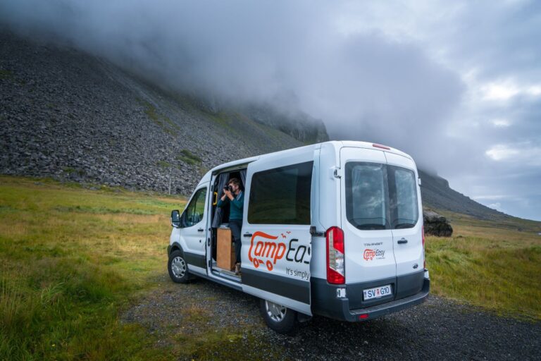 A campervan parked on a gravel road with mountains and clouds in the background, set in Iceland's scenic landscape.