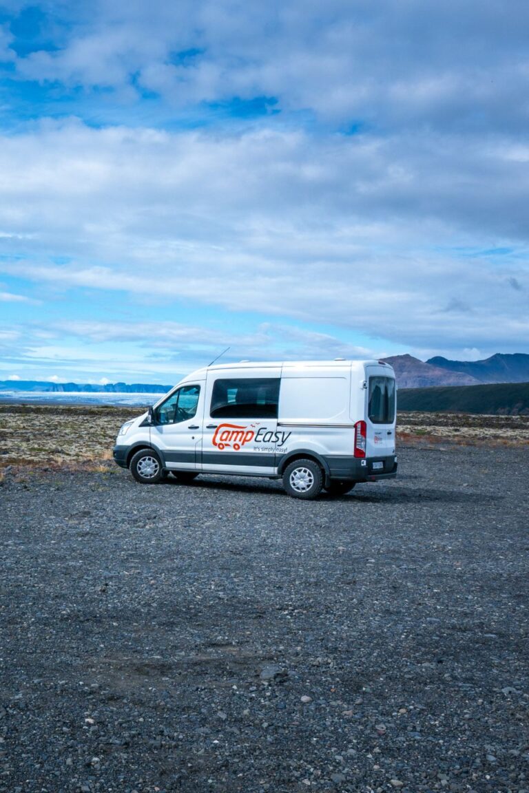 A white campervan parked on a gravel road in Iceland, surrounded by mountains in the background.
