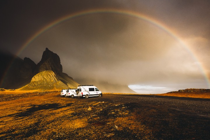 A CampEasy camper vans parked in a dramatic Icelandic landscape with a rainbow arching over dark, moody skies.