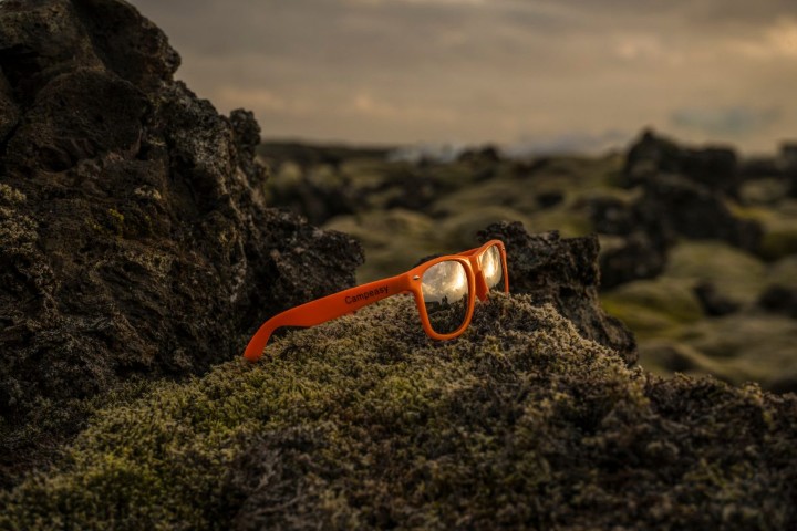 A pair of orange CampEasy sunglasses resting on a moss-covered rock in the Icelandic wilderness.