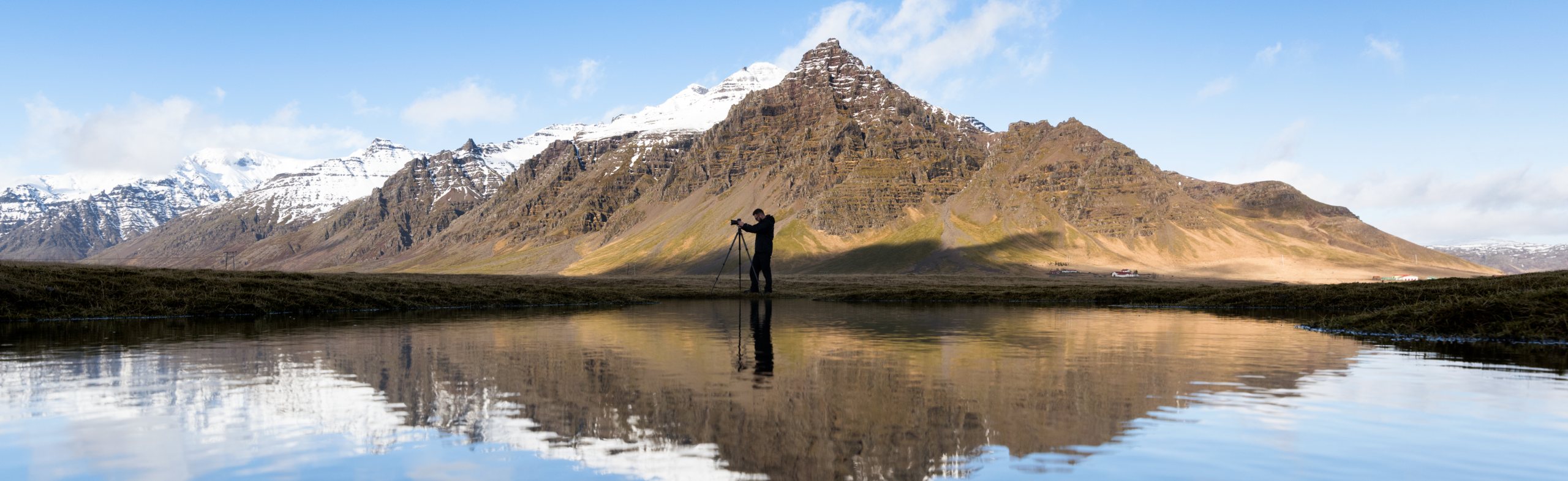 A photographer capturing the majestic snow-capped mountains of Iceland, reflected in a calm lake below, with clear blue skies overhead.