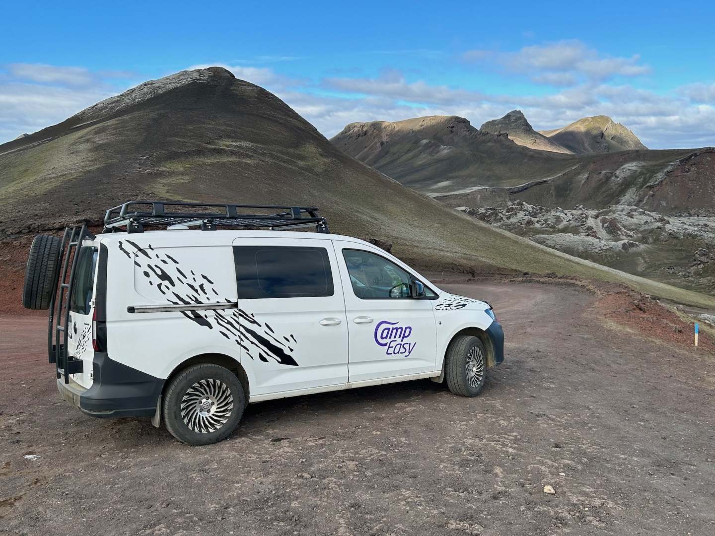 CampEasy campervan parked on a dirt road with vibrant volcanic hills in the background, showcasing the vehicle's adventure capabilities in Iceland's unique geological settings.