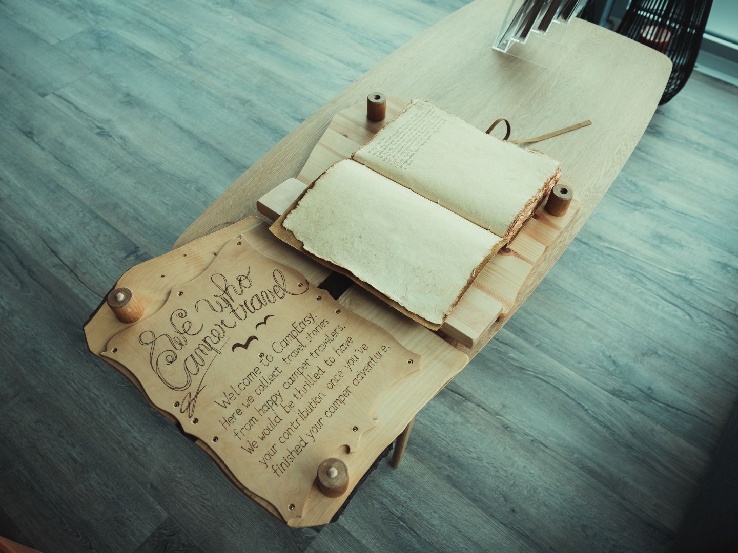 An open book displayed on a wooden stand with a sign that reads 'See Who Camper Travel' and a welcoming message for collecting travel stories from happy campers at CampEasy.