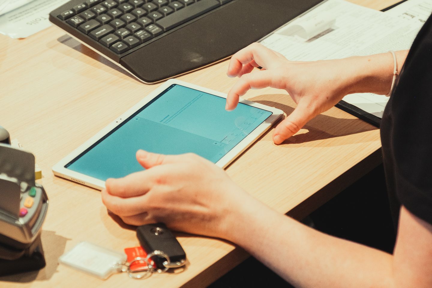 A close-up of a person's hands using a tablet on a desk, with car keys and a card reader nearby, highlighting the digital and modern service approach at CampEasy.