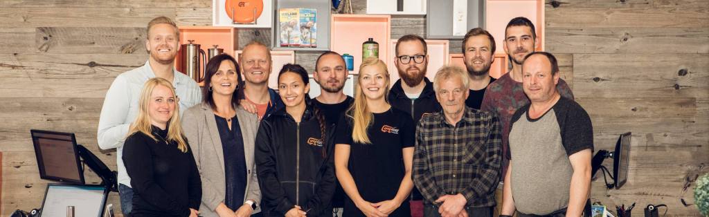 A group photo of the CampEasy team standing together in front of a wooden wall. The team members are smiling and appear friendly, with some wearing CampEasy branded clothing. Behind them are shelves displaying various camping gear and brochures.