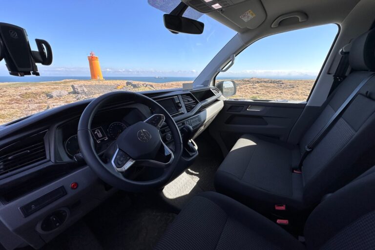 Interior of the front of a campervan, showcasing a scenic ocean view through the windows.