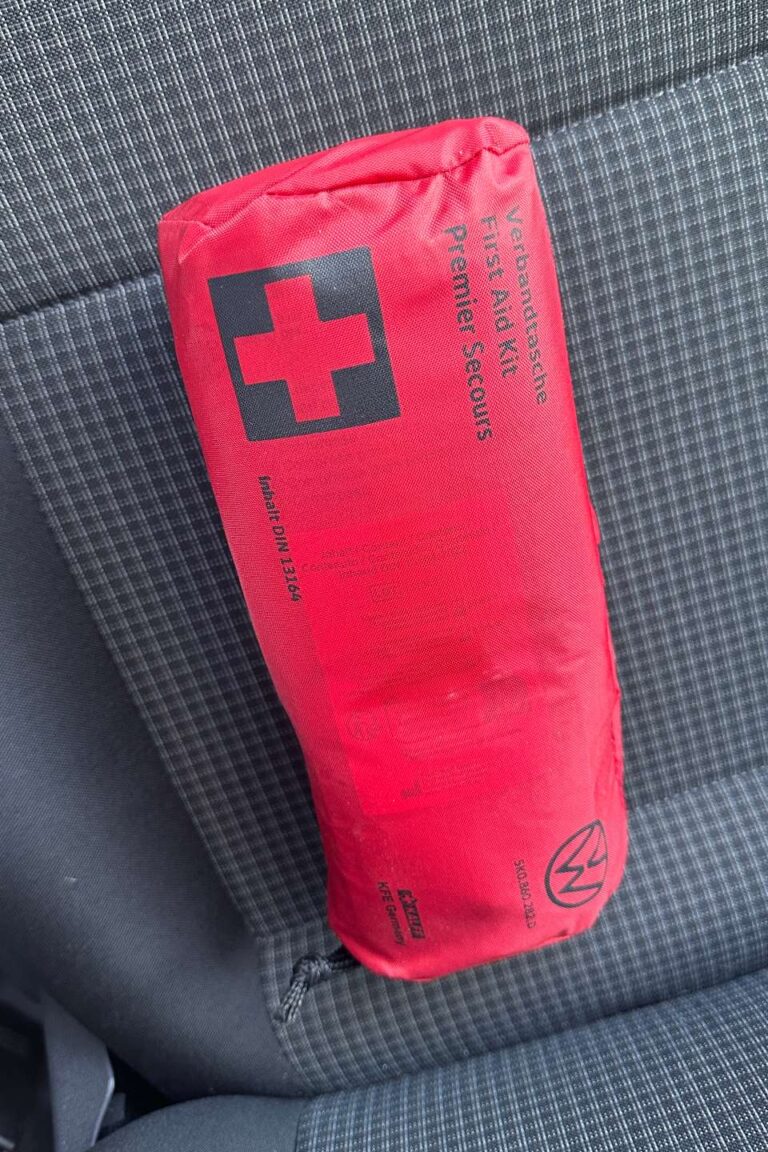 A red first aid kit lying on a gray seat.