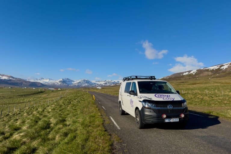 A campervan parked on the road surrounded by green fields with mountains in the background.