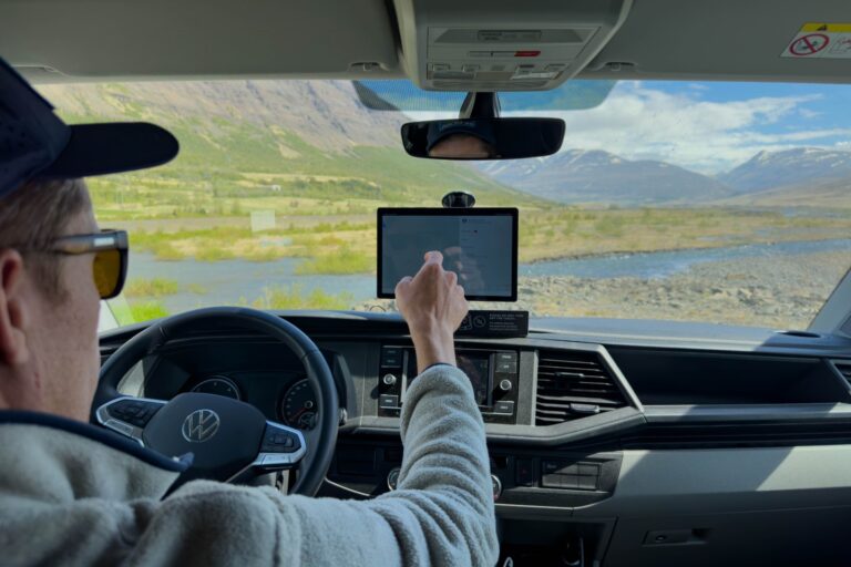 A man sits behind the wheel of a camper van and looks for something on a tablet.