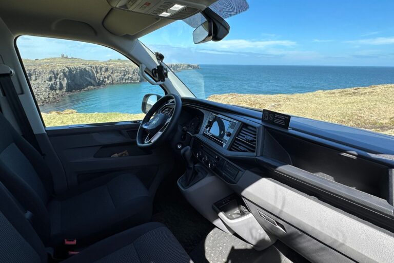 Interior of the front of a campervan, showcasing a scenic ocean view through the windows.