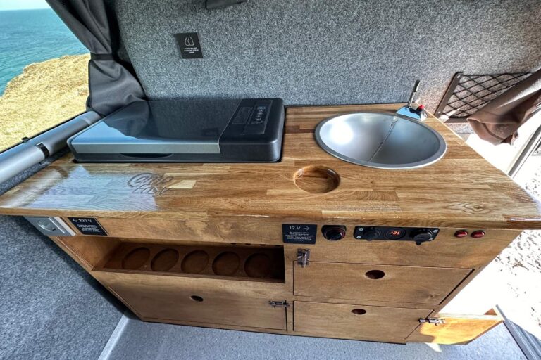 A kitchenette inside the campervan, including a sink, fridge, and shelves with cabinets.