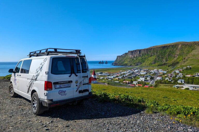 A campervan parked in a gravel lot on a hill outside the town of Vik.