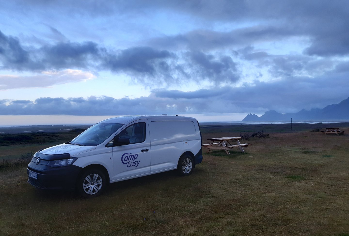 CampEasy campervan parked at a remote picnic area overlooking a vast landscape with distant mountains under a dramatic cloudy sky, perfect for peaceful escapes in Iceland's wilderness.