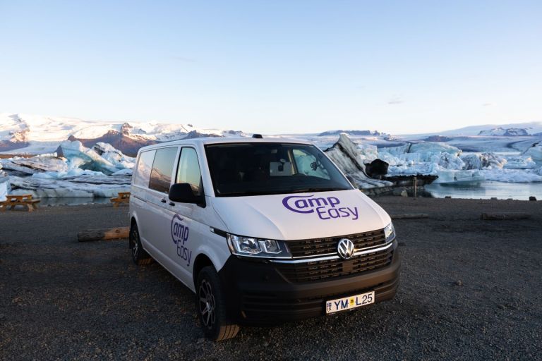 White camper van parked on the rocky parking with wooden benches next to the iceberg lagoon in Iceland.