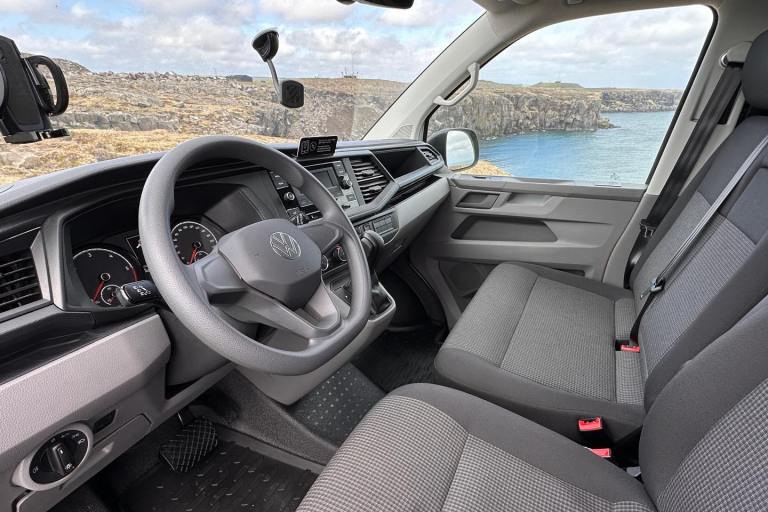 Interior of campervan in Iceland, showing passenger's seat and dashboard with scenic rugged landscape and the sea outside