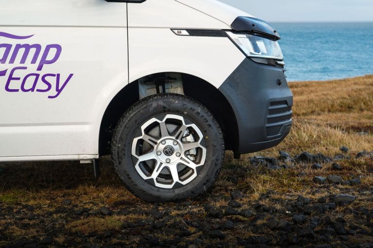White camper van with "CampEasy" logo parked on rugged terrain in Iceland near the ocean and grassy landscape