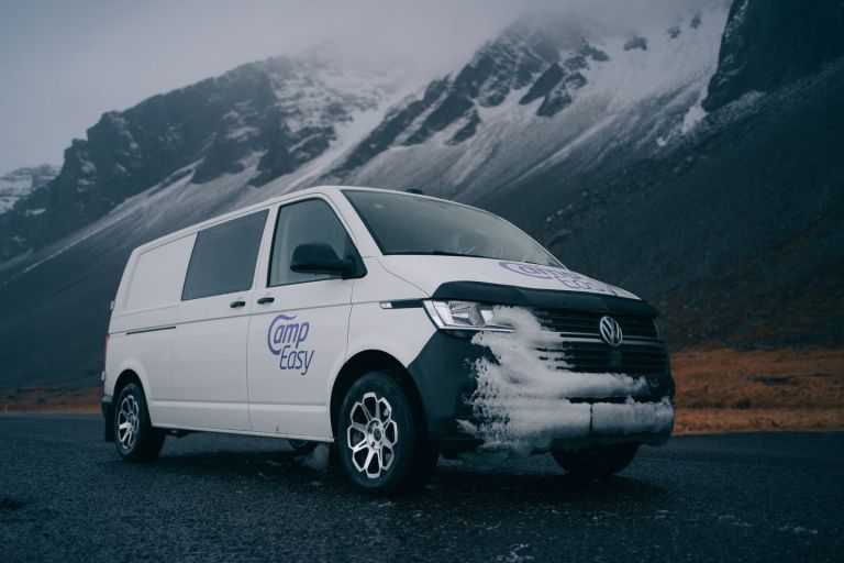 White 'Camp Easy' campervan parked on a road with misty and snowy mountains in the background.