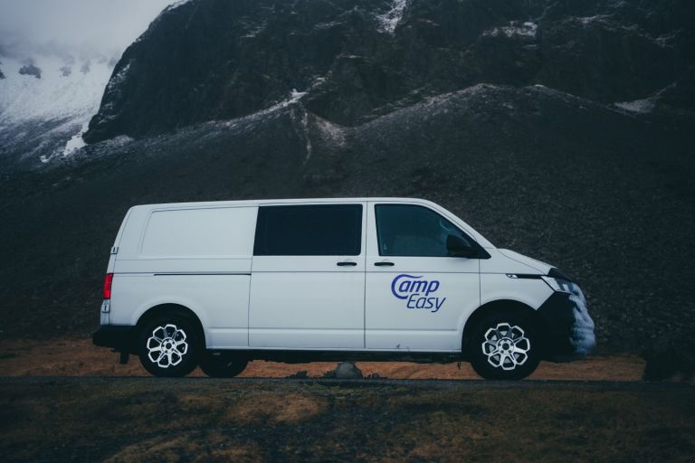 White 'Camp Easy' campervan parked on a snowy road with rugged mountains in the background.