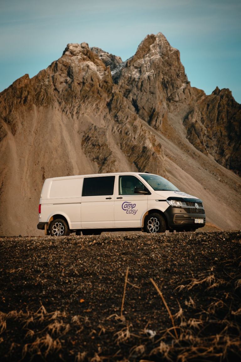 Camper van parked on the gravel road next to the huge mountains in the background.