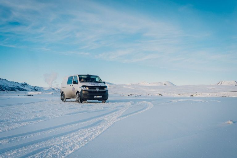 White 'Camp Easy' campervan driving on a snowy road with mountains under a clear blue sky in Iceland.