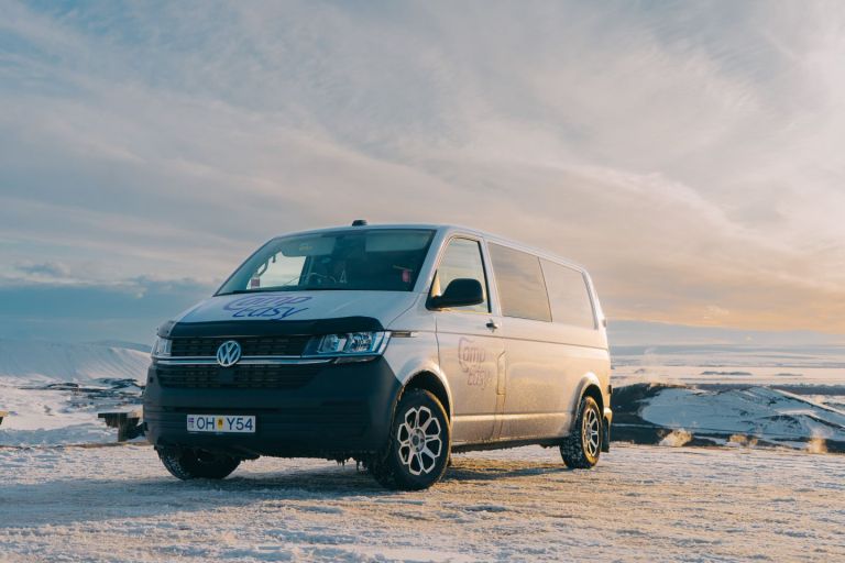 White 'Camp Easy' campervan parked on a snowy landscape with mountains under a colorful sky at sunrise.