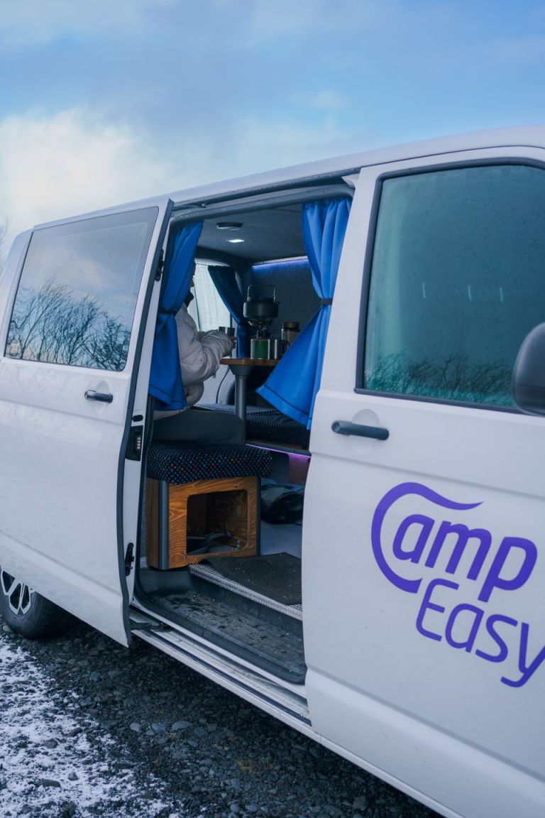 A person is cooking the water for a drink inside the campervan with open back and side doors.