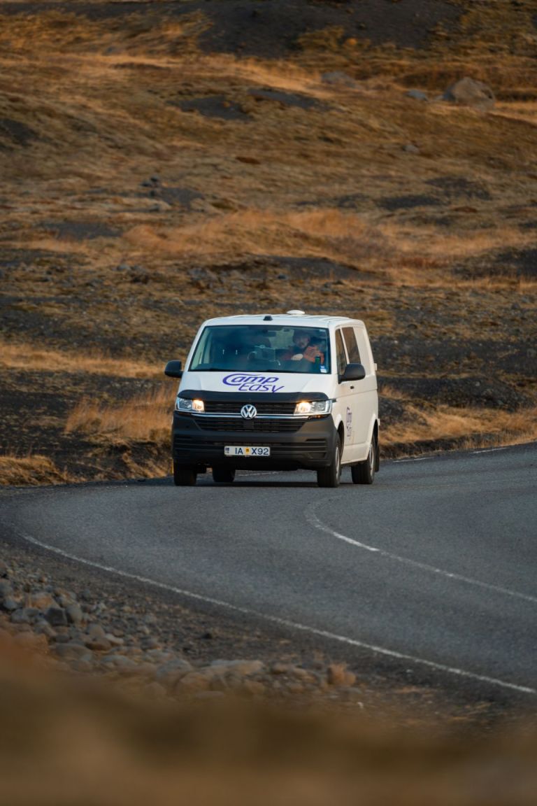 A man is driving the campervan on the road surrounded by rugged Icelandic terrain.