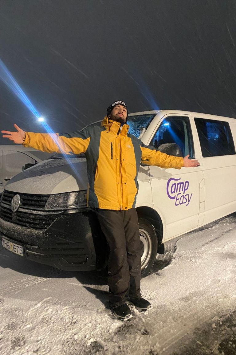 A man with yellow jacket leaning on the front of the campervan with spread out arms.