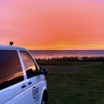 CampEasy campervan parked at a coastal site during a vibrant sunset, with stunning shades of pink and orange lighting up the sky and reflecting off the van, capturing a breathtaking moment in Iceland.